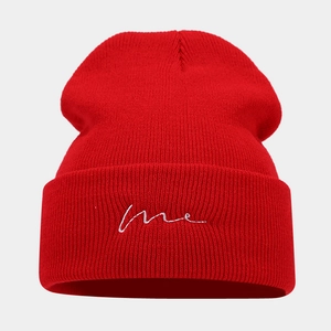 Detailed close-up of red ribbed beanie with white handwritten me embroidery on the cuff
