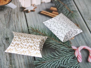 Christmas pillow boxes with silver and gold vine patterns on a rustic wooden table