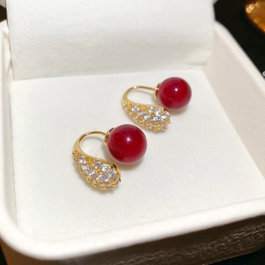 Detail of red bead earrings with clear crystals and gold plating on velvet cushion