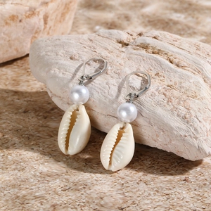 Close-up of shell and pearl earrings on natural stone for beach vacation style