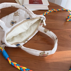 Detail view of quilted floral bear phone bag featuring colorful woven rainbow shoulder strap