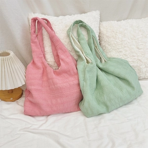 Detail shot of textured fabric tote bags in pink and mint green on a cozy sofa