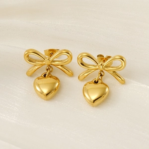 Détails macro de boucles d'oreilles nœud dorées avec cœurs sur fond de tissu doux