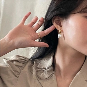 Close-up of a model wearing elegant large pearl drop earrings and a minimalist gold ring