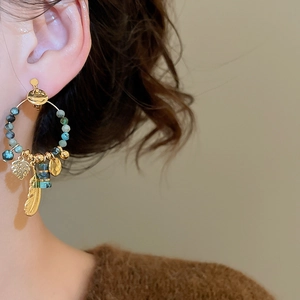 Close-up of bohemian earrings featuring gold feathers and blue stone beads on model