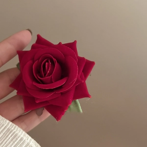 Detailed close-up of dark red velvet rose hair clip with green leaves in hand