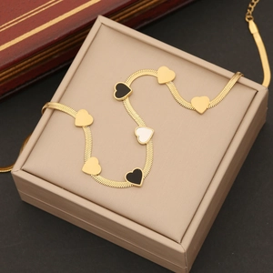Goldene Schlangenkette mit bunten Herzanhängern auf einer beigen Schmuckschatulle