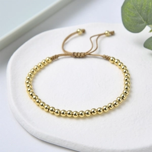 Detail eines verstellbaren geflochtenen Armbands mit polierten Goldperlen auf Stein