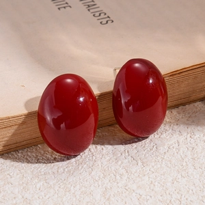 Macro detail of oval deep red resin earrings on a vintage book with elegant shadows