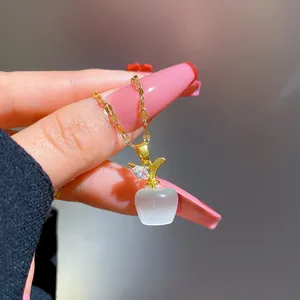 Macro view of gold plated apple necklace featuring a white cat eye stone and crystal leaf