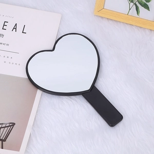 Close-up of black heart-shaped handheld mirror with handle on white plush surface