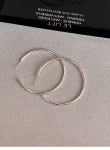Flat lay of silver polished C-shaped hoop earrings on light gray textured background