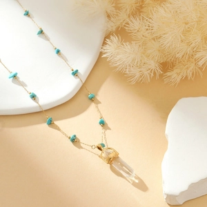 Elegant gold necklace with blue turquoise beads and clear crystal pillar on a warm backdrop
