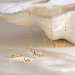 Close-up of elegant gold LOVE letter jewelry set featuring two necklaces and earrings