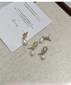 Detailed view of knot metal earrings with drop pearls on beige textured background
