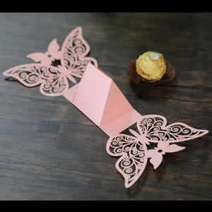 Detail of pink laser-cut butterfly wedding favor box with a chocolate for scale