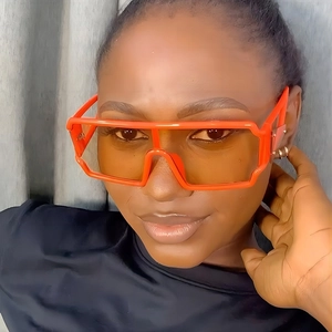Front view of model wearing bright orange oversized wraparound punk sunglasses with flat top