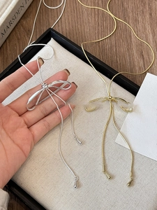 Close-up of bow-shaped necklaces in gold and silver finish with elegant drop pendants