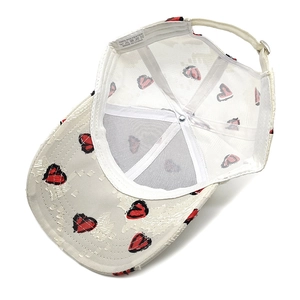 Detail view of white baseball cap showing 100% polyester fabric and red heart embroidery