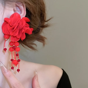 Close-up of red fabric flower earrings with beaded tassels worn by a fashion model