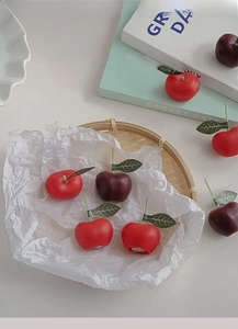 Detalle de velas perfumadas con forma de cereza en una cesta con hojas naturales