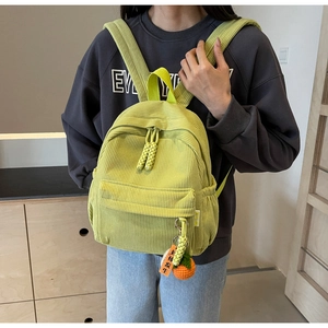 Detail showing grass green corduroy mini backpack texture and decorative persimmon pendant