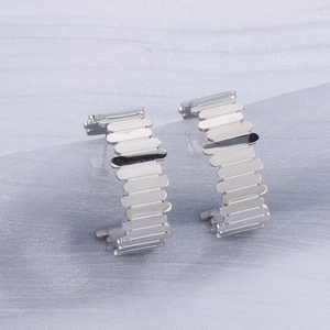Détail de boucles d'oreilles demi-cercles argentées avec texture industrielle