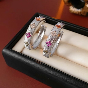 Gros plan de boucles d'oreilles en C argentées avec trèfles en zircon colorés dans un coffret