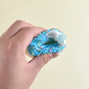 Blauer Donut-Stressball mit bunten Streuseln wird auf gelbem Hintergrund mit der Hand gedrückt