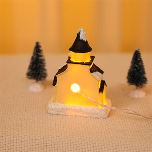 Close-up of a glowing miniature Christmas house with warm LED lights and artificial snow
