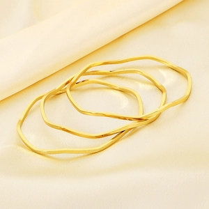 Detail of three stacked wavy gold bangles on soft silk fabric highlighting metallic texture