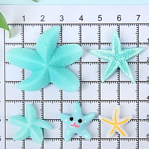 Size comparison of resin starfish charms in mint and blue on grid paper with metric ruler