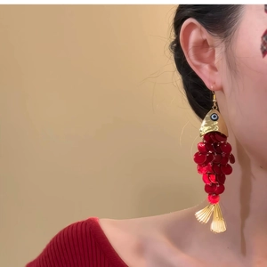 Macro view of fish-shaped earrings featuring red sequins and golden metallic accents