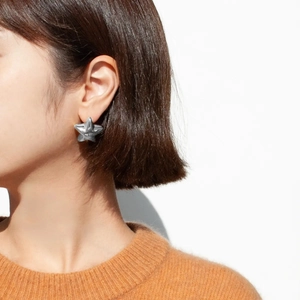 Detailed view of a silver 18k stainless steel star earring worn by a model