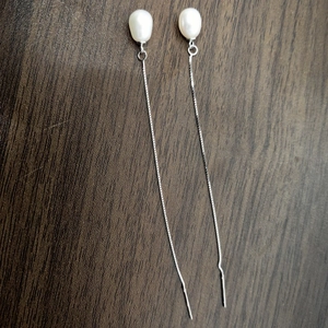 Detailed close-up of water drop pearl earrings with long silver tassels on wood