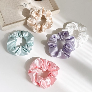 Flat lay of multiple pastel satin scrunchies showing glossy silk texture and vibrant colors