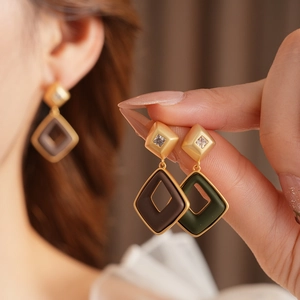 Close-up of diamond-shaped gold earrings with brown and green accents on female model