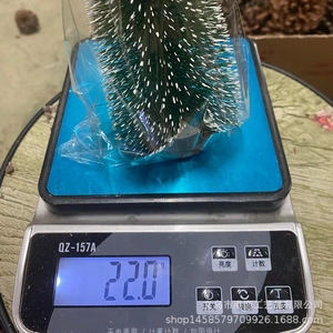 Mini snowy Christmas tree decoration weighing 22g on a scale for product specification