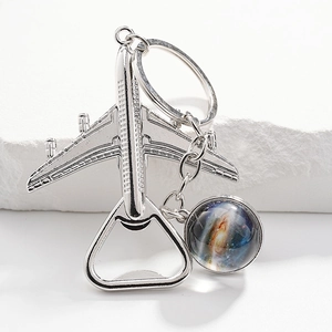 Detail of silver airplane bottle opener keychain with a galaxy pendant on white stone