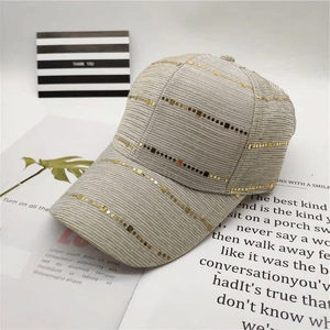 Detail of light beige baseball cap featuring rows of gold sequins on a textured fabric