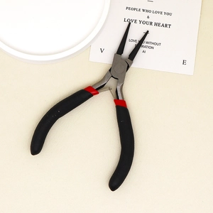 Detail of round nose jewelry pliers with ergonomic black and red handles on a beige surface