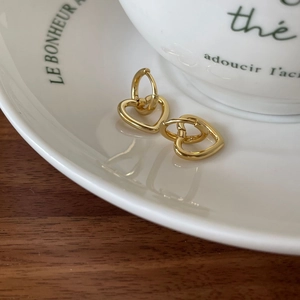 Detailed view of heart-shaped gold stud earrings on a white ceramic tray and wood surface