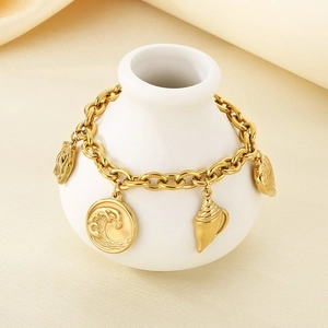 Detail of gold nautical charm bracelet with wave and shell pendants on white ceramic vase