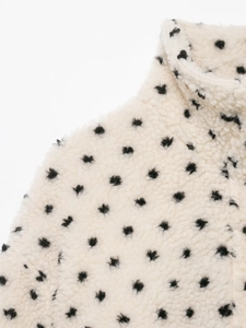 Gros plan d'une veste en polaire blanc cassé à pois noirs avec un col montant épais