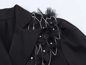 Détail d'épaule de blazer noir avec fleurs en tissu, chaînes de perles et strass brillants