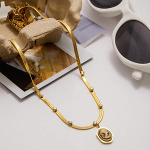 Close-up of a gold snake chain necklace with an oval portrait relief pendant