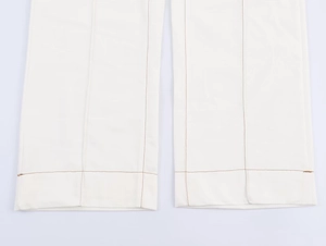 Detail of high-waisted flared trousers with brown contrast stitching on white hems