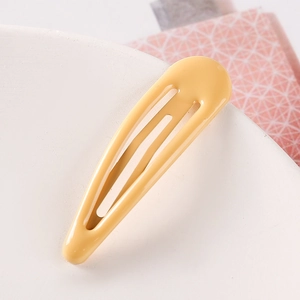 Macro close-up of a glossy yellow teardrop-shaped metal hair clip on a white dish