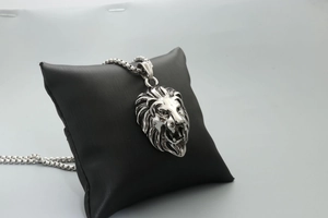 Detailed macro view of silver lion head pendant with box chain on black display