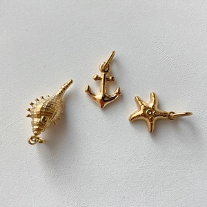 Detailed close-up of gold stainless steel ocean pendants featuring seashell, anchor, and starfish